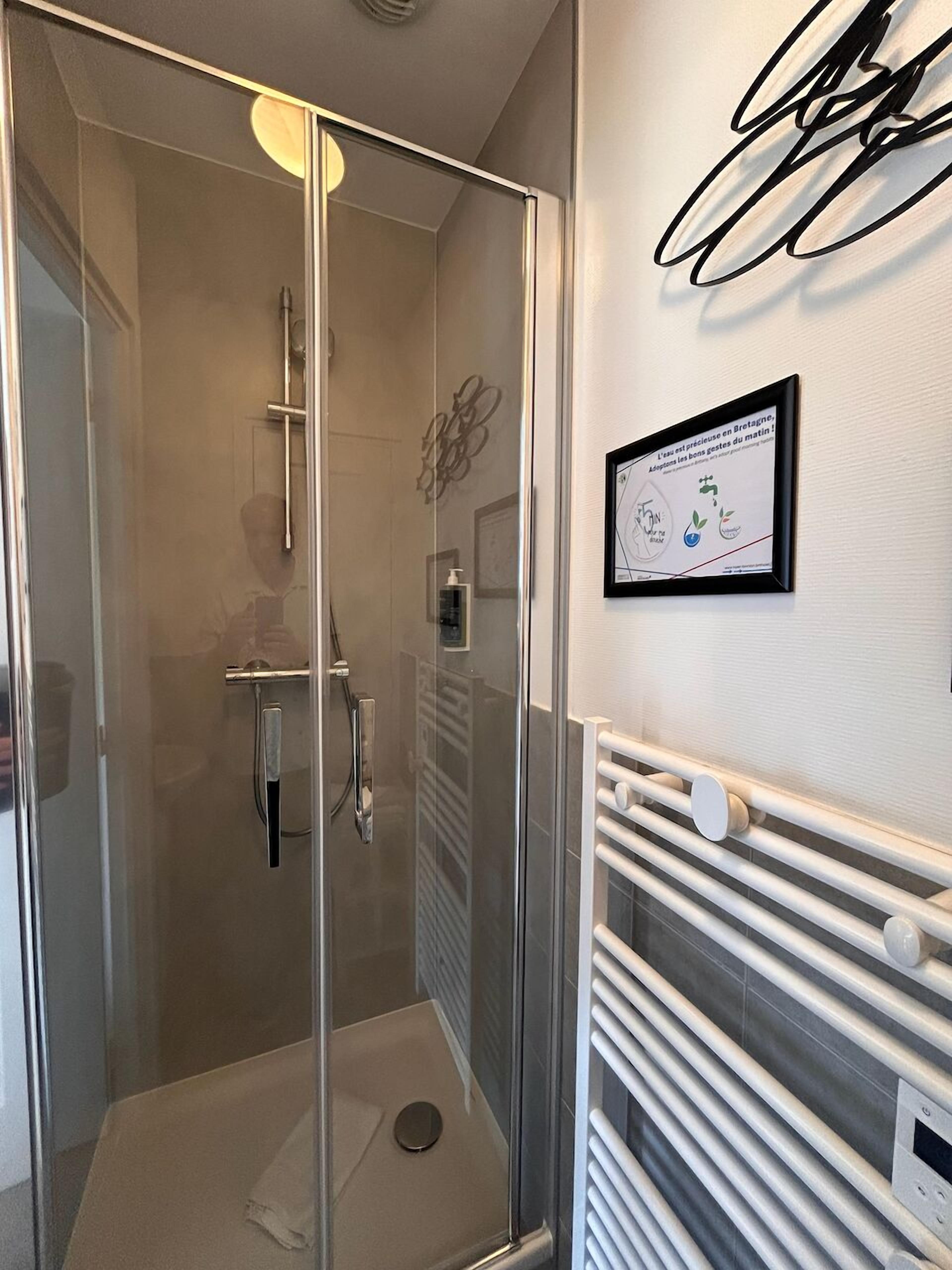 Un baño moderno con cabina de ducha de vidrio, un cartel informativo enmarco y un perchero para toallas.