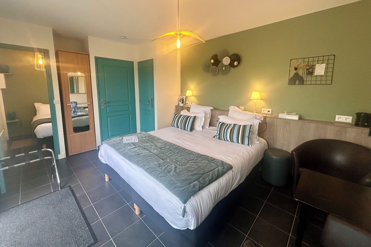 Een hotelkamer met een groot bed, twee nachtkastjes met lampen, een stoel, een spiegel en een groene muur met decoratieve borden.