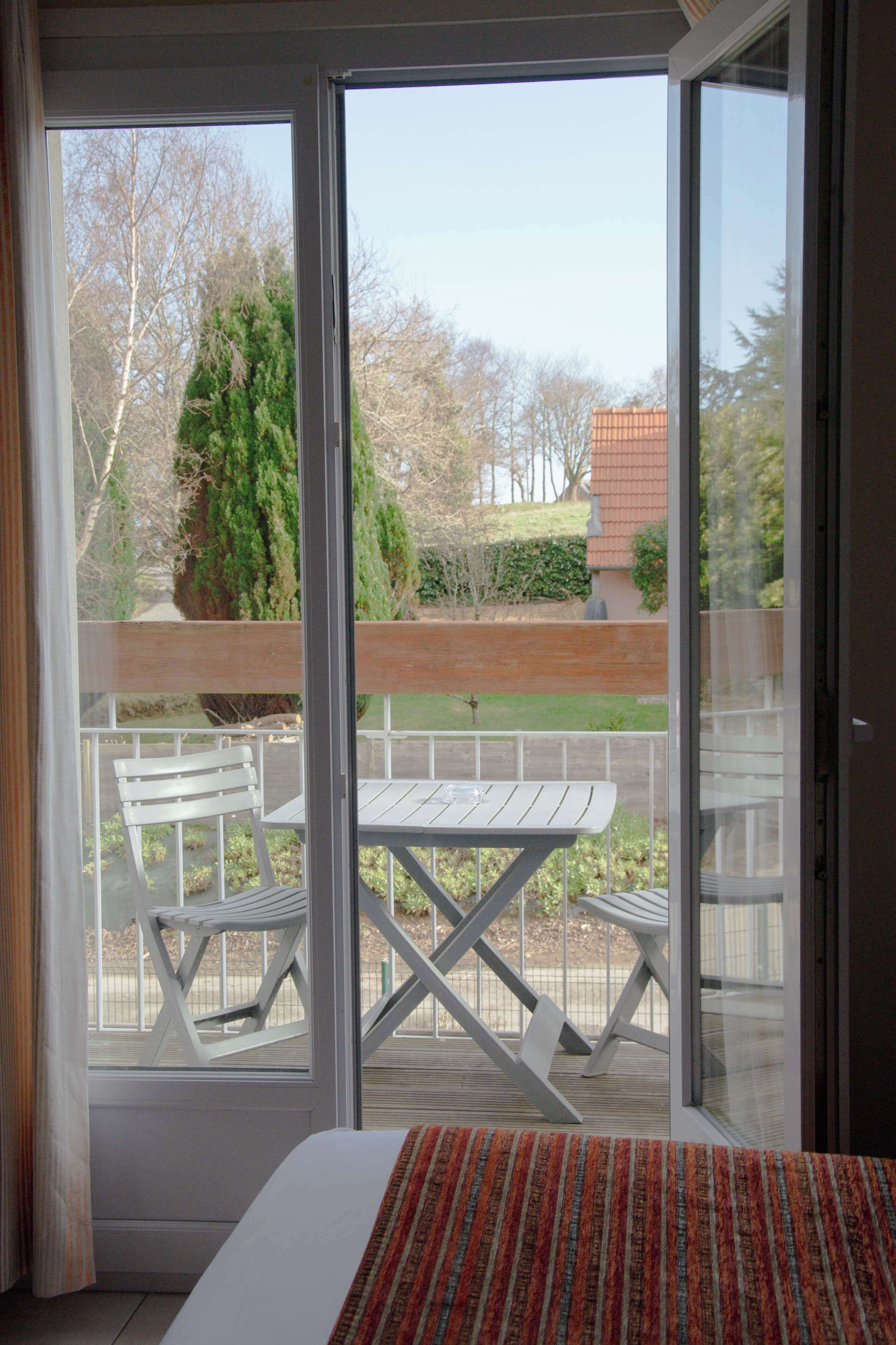 Una habitación con un amplio ventanal corredero que da a una terraza exterior con una mesa blanca y dos sillas.