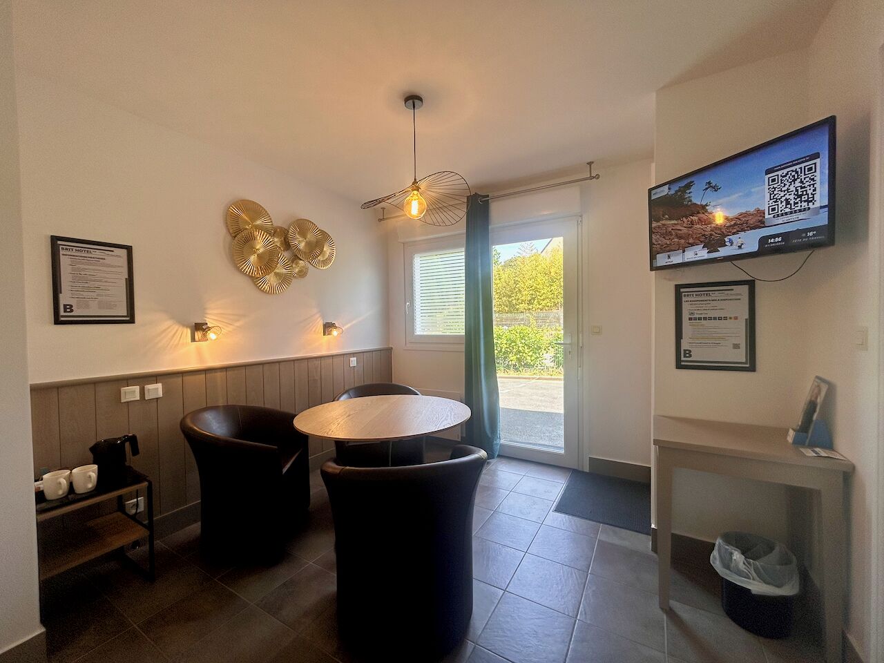 A modern kitchen with a round table, two black chairs, a ceiling fan, and a TV mounted on the wall.
