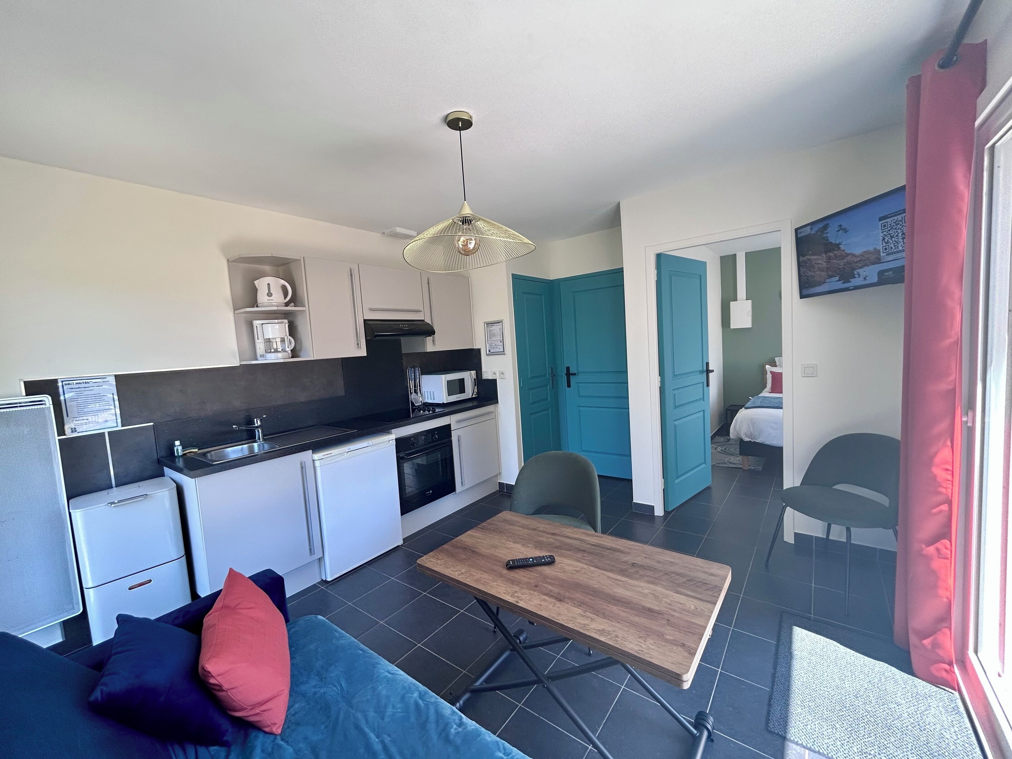 Een compacte keuken met moderne apparaten, een eethoek met een houten tafel en een woonruimte met een bank en stoelen.