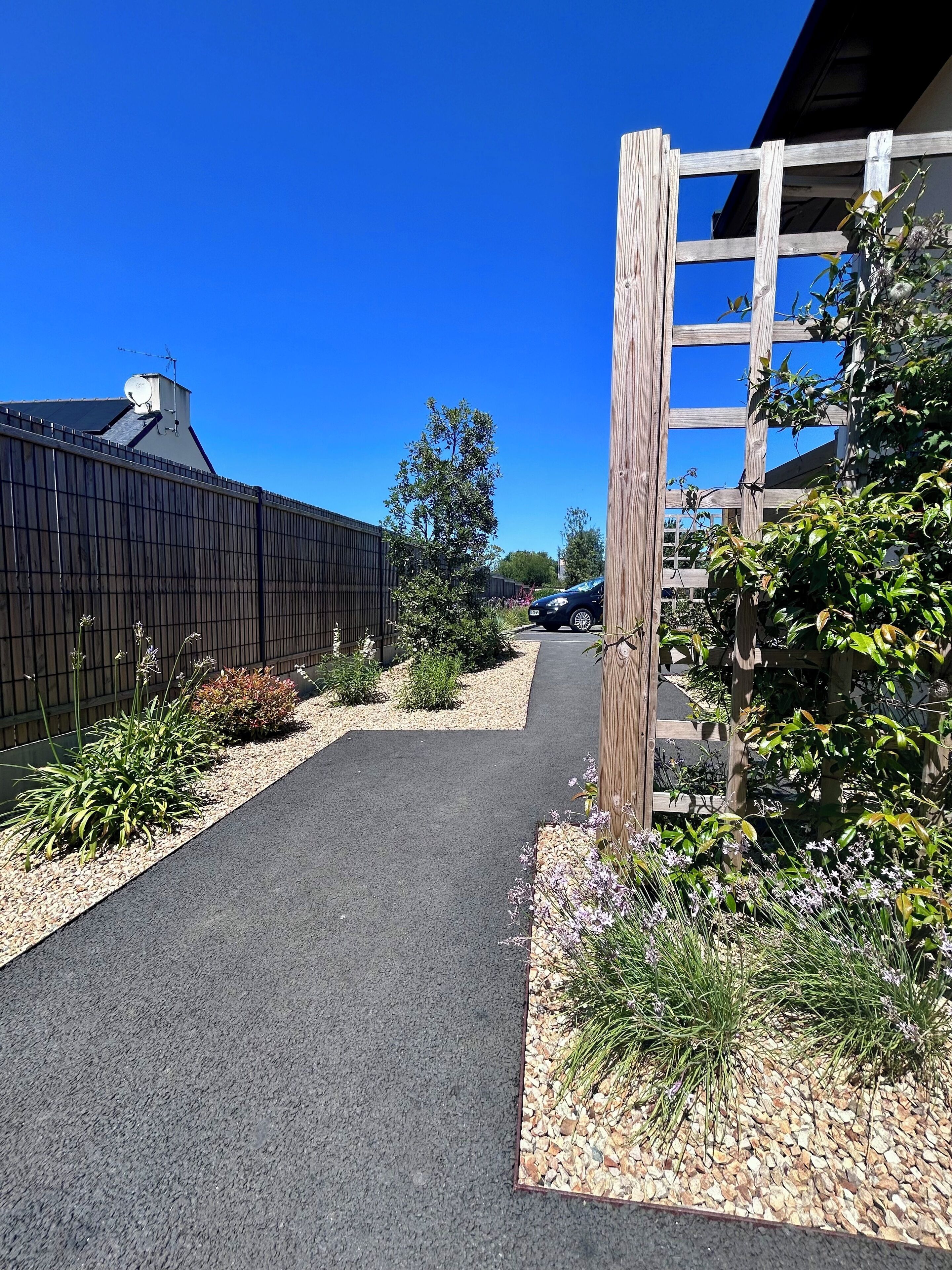 A pathway leading to a building with a wooden fence and a car parked nearby.
