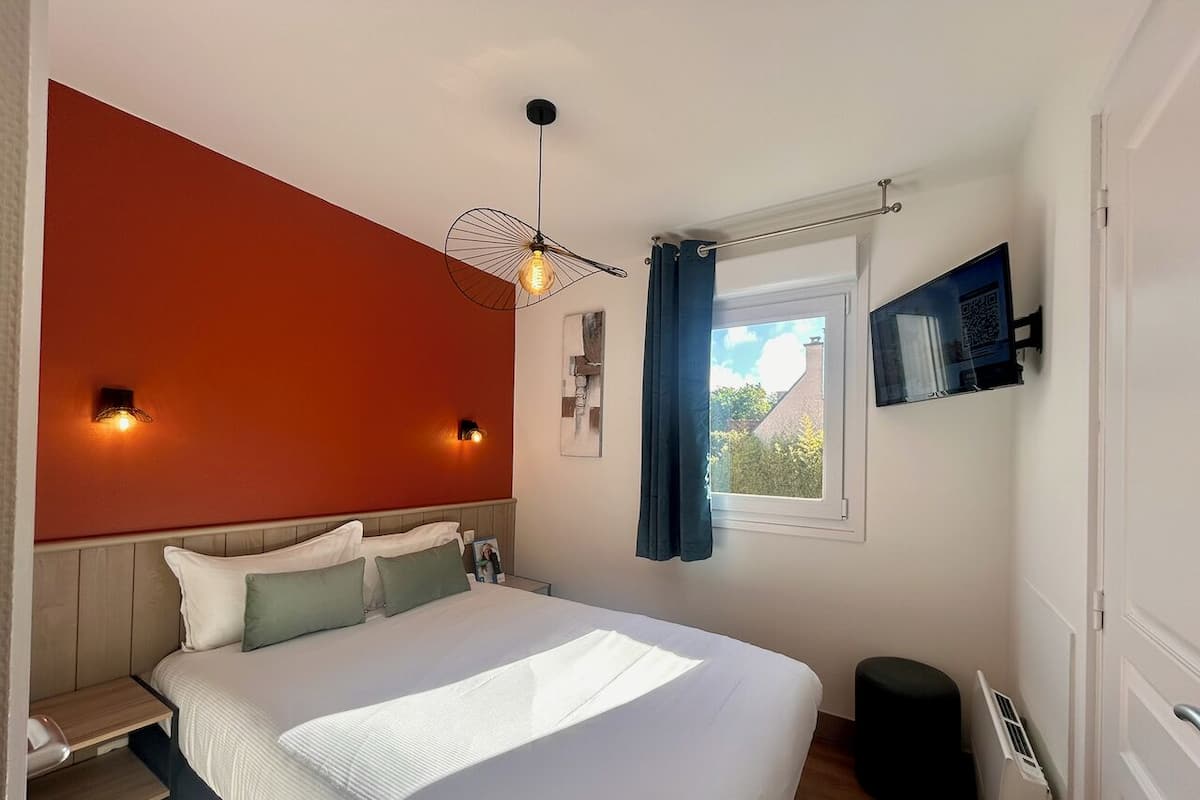 Een slaapkamer met een bed, nachtkastjes, een raam met gordijnen, een tv aan de muur en een radiator.
