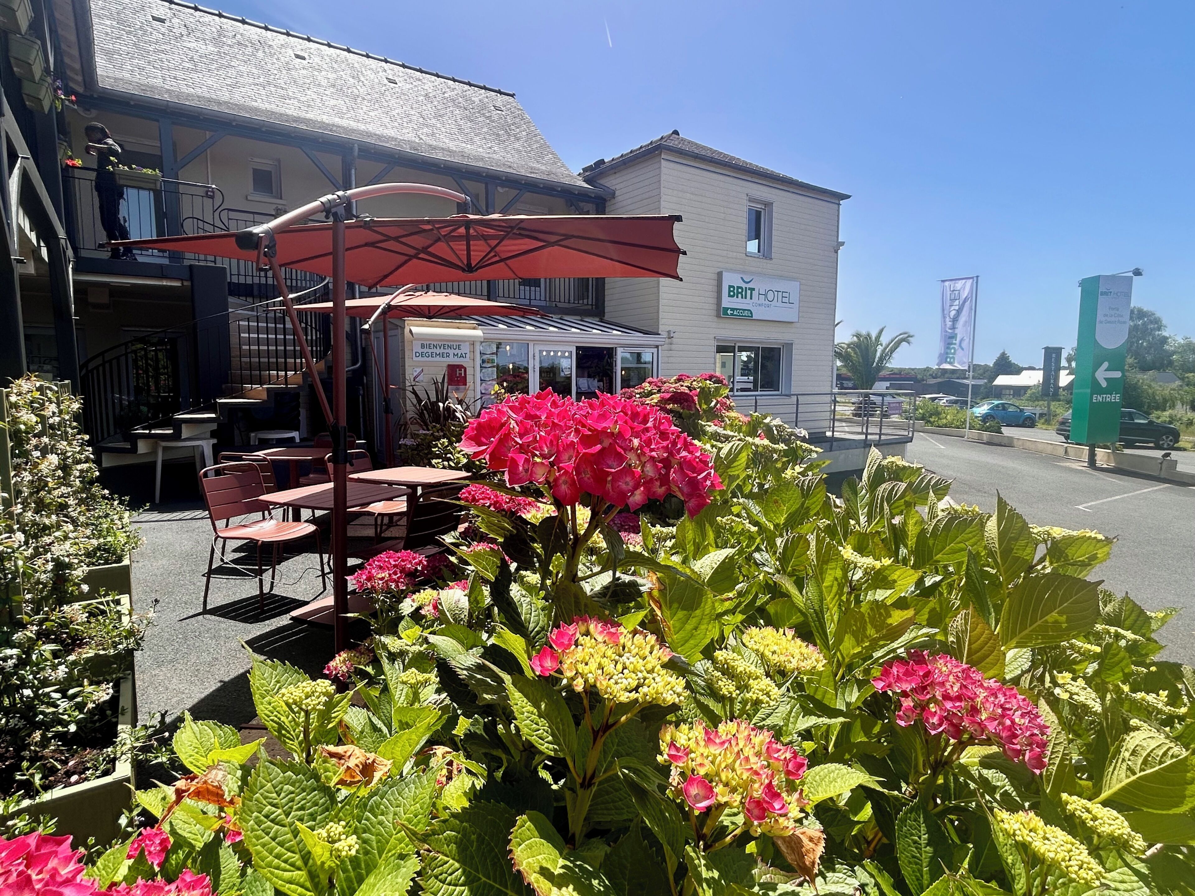 Un hôtel doté d’une terrasse, une enseigne indiquant « BRIT HOTEL », et un ciel dégagé.