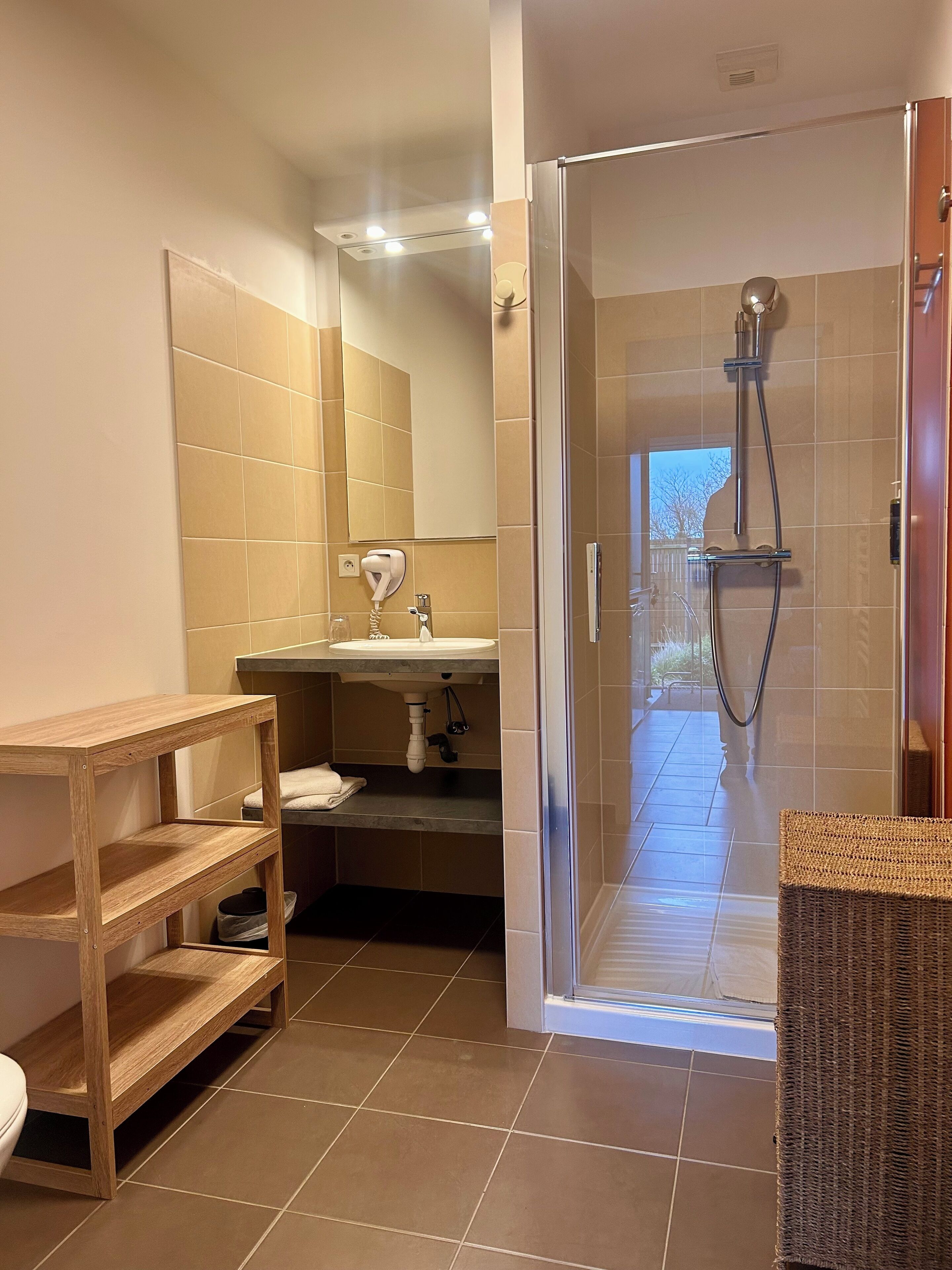 A bathroom with a wooden shelf, a sink, a mirror, and a shower area.