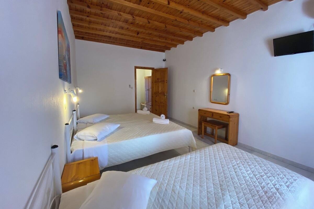 Habitación de hotel con dos camas, techo de madera, televisor, espejo y un pequeño escritorio de madera.