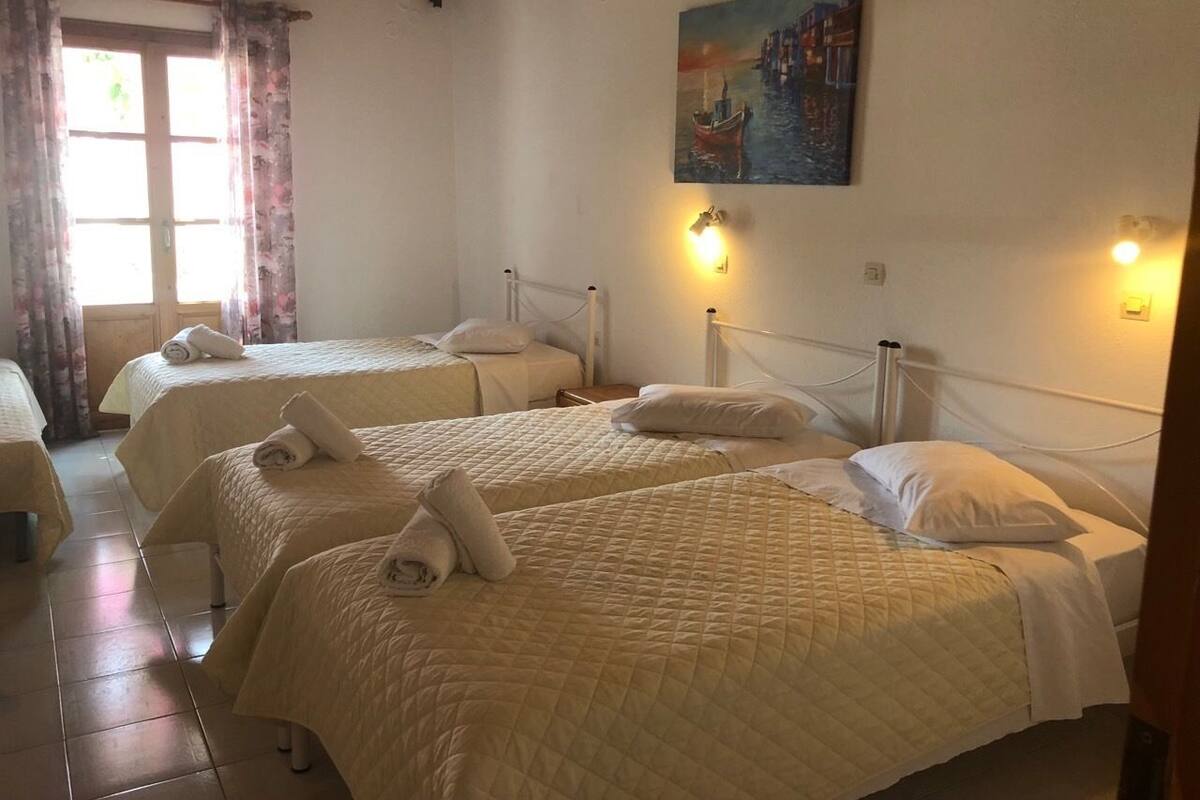 Habitación de hotel con tres camas, cada una con una toalla enrollada, un cuadro en la pared y dos luces adosadas.