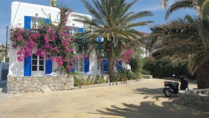 A white building with blue shutters and pink bougainvillea flowers, a stone wall, and a parked scooter. - Anemos Studios & Apartments (Mykonos)