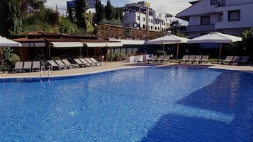 Una piscina al aire libre, sombrillas, sillones reclinables de piscina