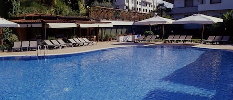 Una piscina al aire libre, sombrillas, sillones reclinables de piscina