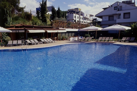 Una piscina al aire libre, sombrillas, sillones reclinables de piscina