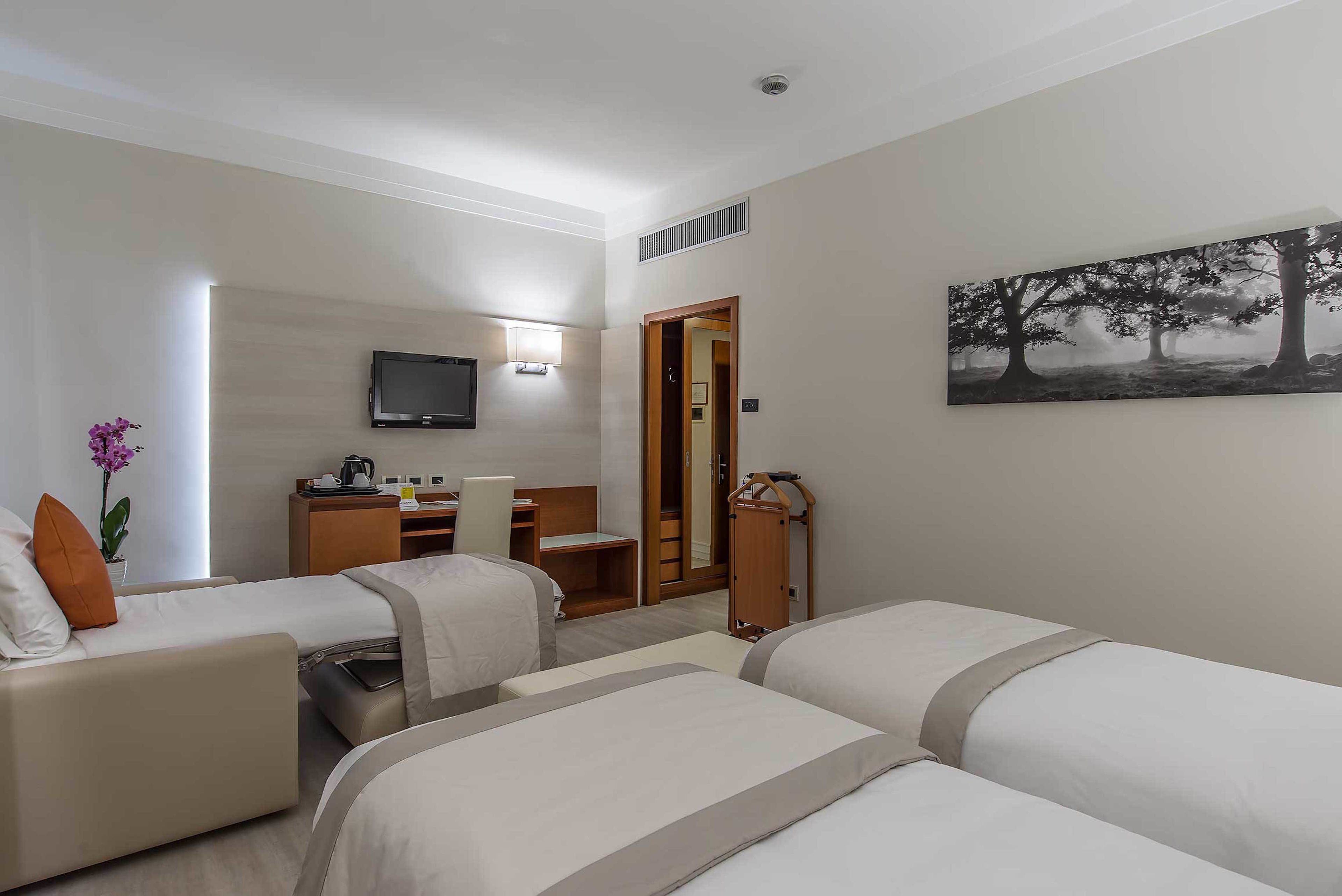 Een hotelkamer met twee bedden, een bureau, een stoel, een televisie en een schilderij aan de muur.