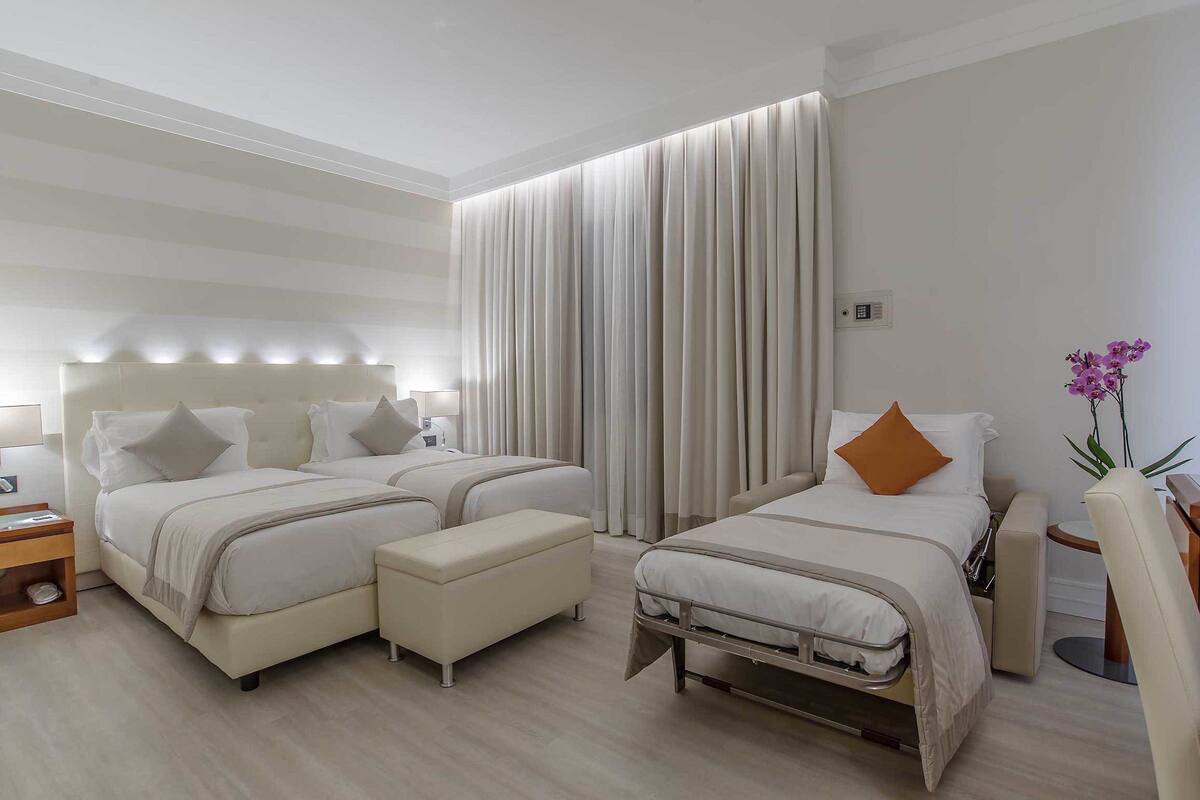A hotel room with two beds, a bedside table, a chair, and a small table with a lamp.
