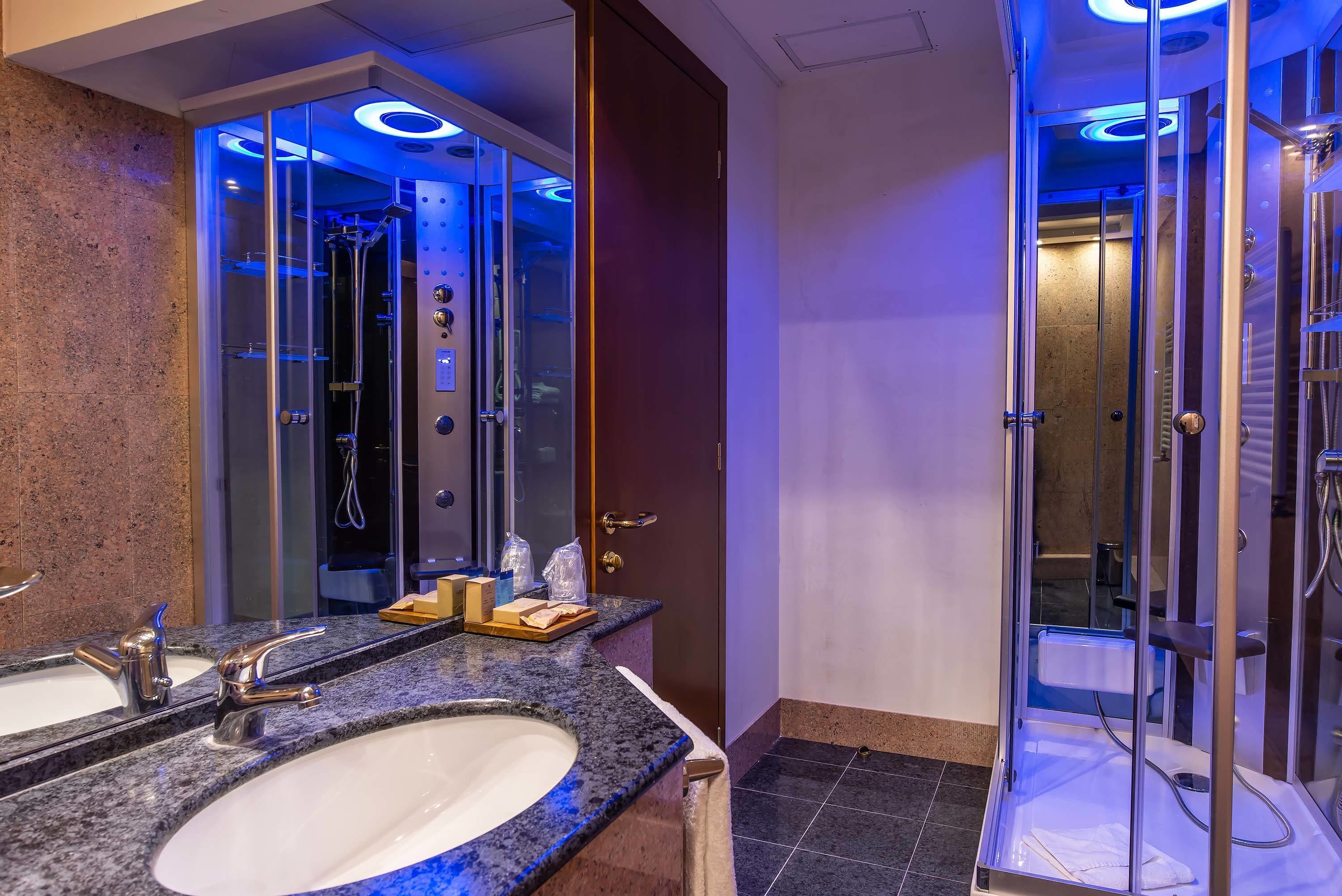 A modern bathroom with a granite countertop, a large mirror, and a glass-enclosed shower area.