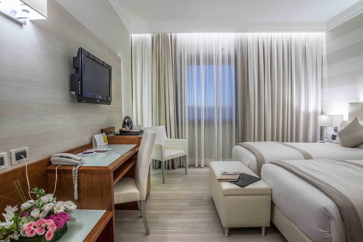 A hotel room with a desk, chair, bed, and a TV mounted on the wall.