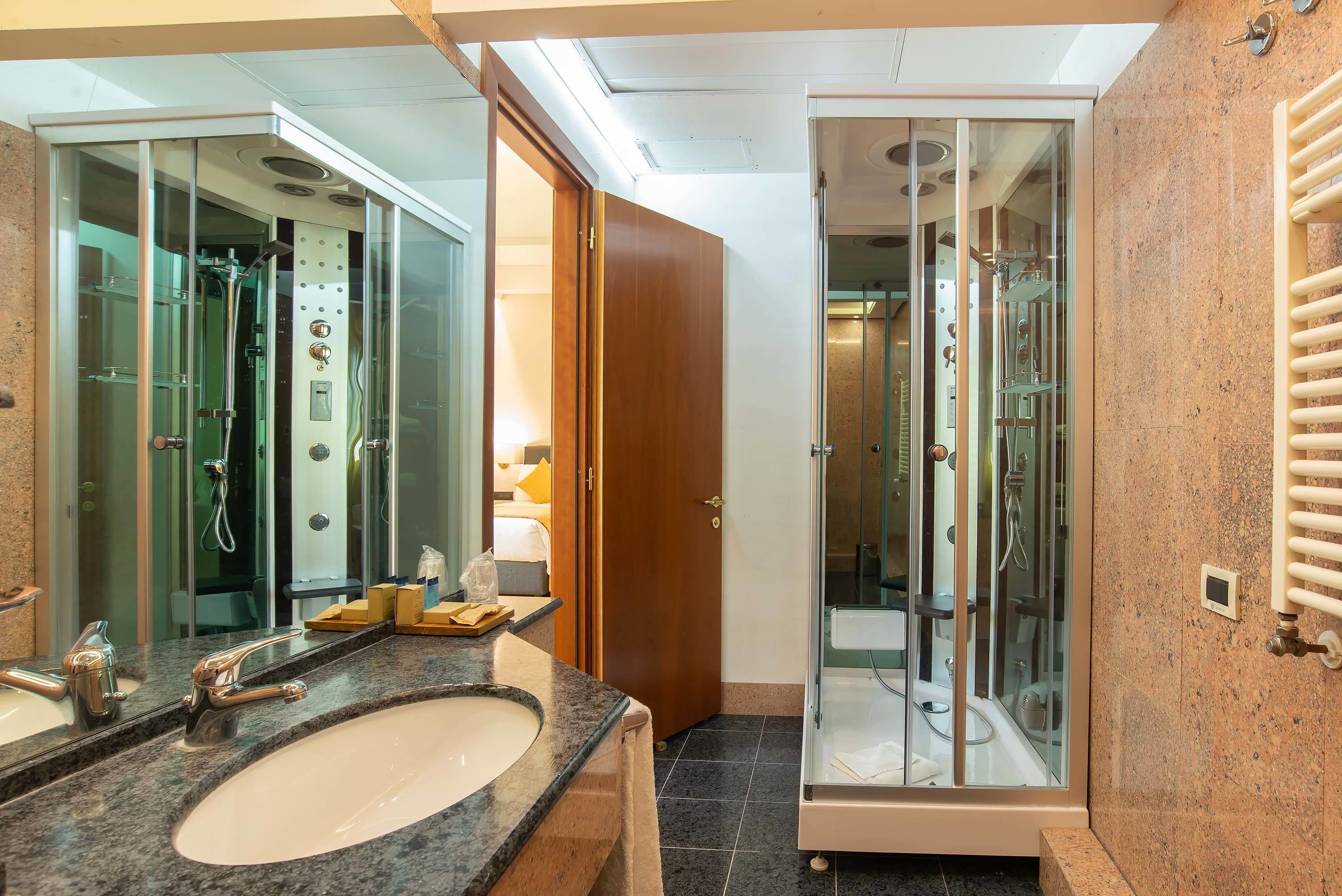 A modern bathroom with a granite countertop, a large mirror, a glass-enclosed shower, and a wooden door.