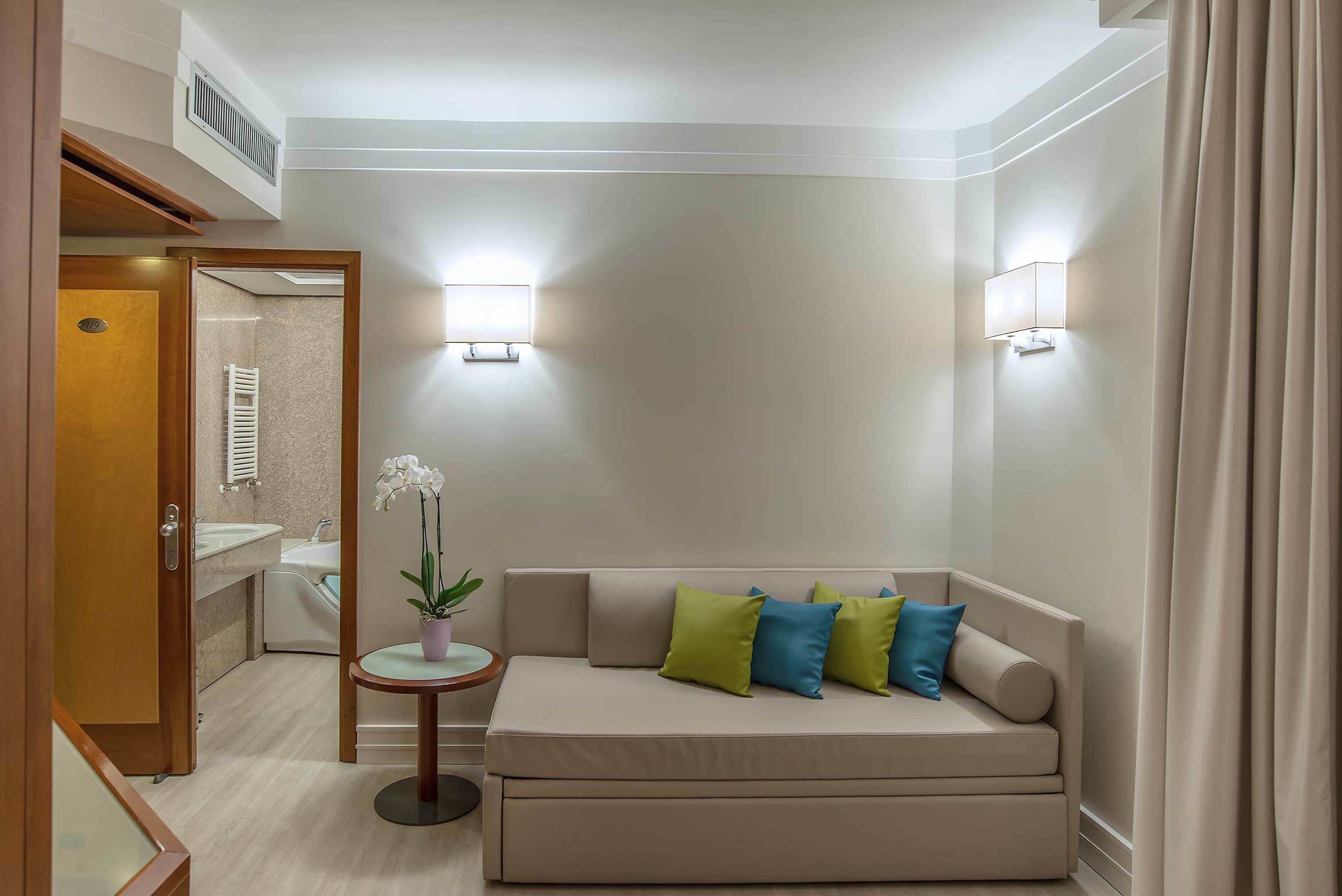 Habitación de hotel moderna con un sofá color beige, una mesita redonda con una orquídea en maceta y dos lámparas de pared.