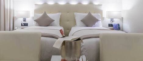 A hotel room with two beds, a minibar, a table with two glasses, and a remote control on the nightstand.