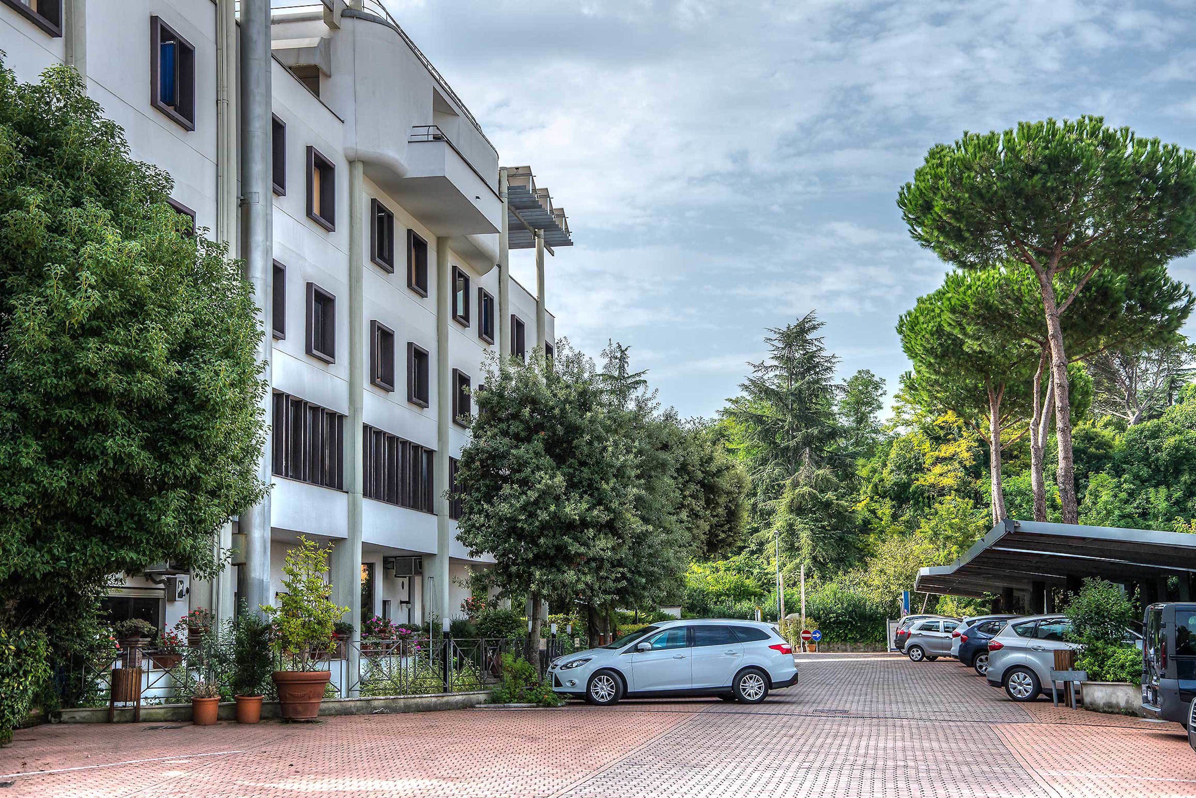 Un hôtel à plusieurs étages doté d’un parking, entouré d’arbres et de plantes en pot.