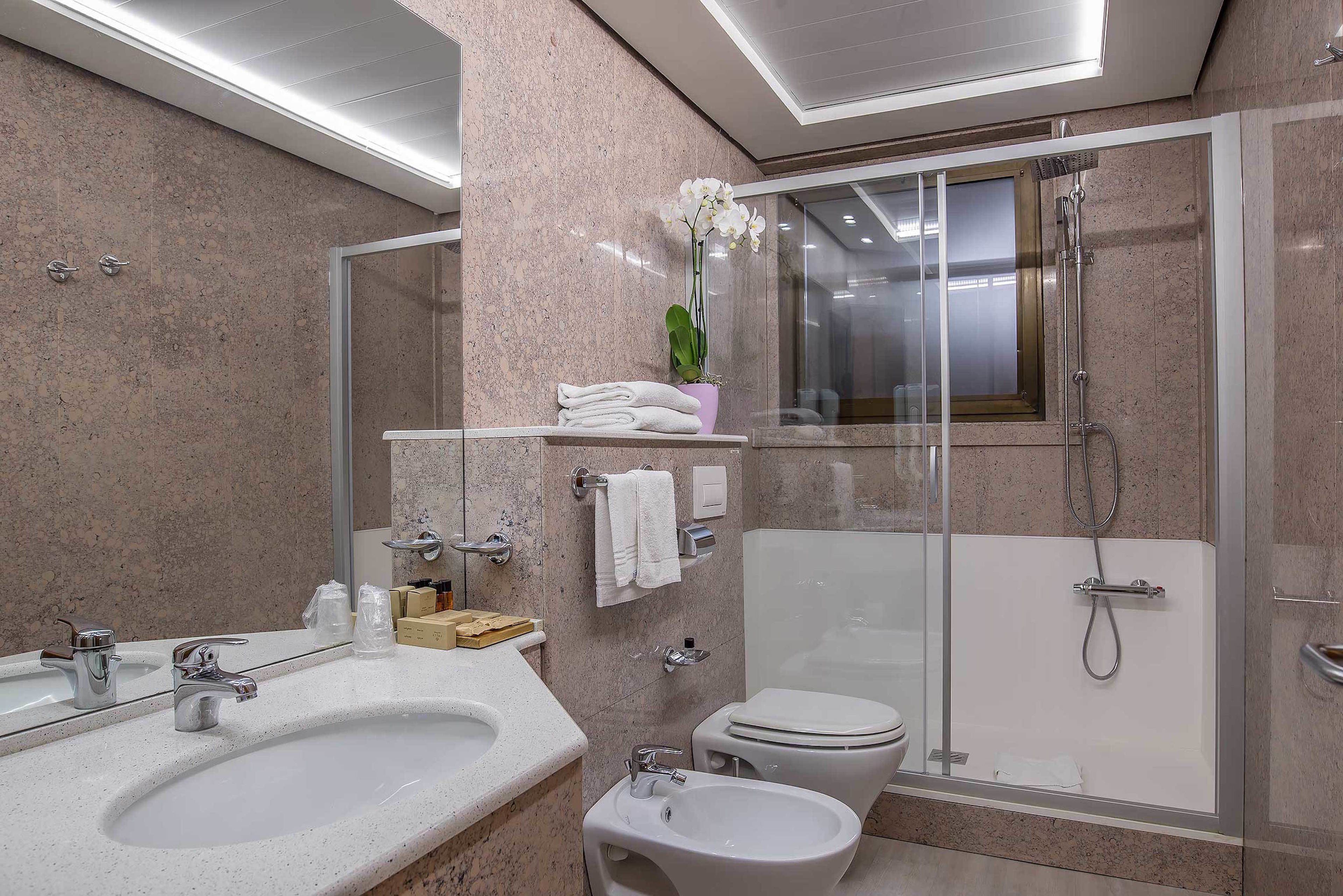 Un baño moderno con un lavamanos grande, bidé, inodoro y ducha con mampara de vidrio.