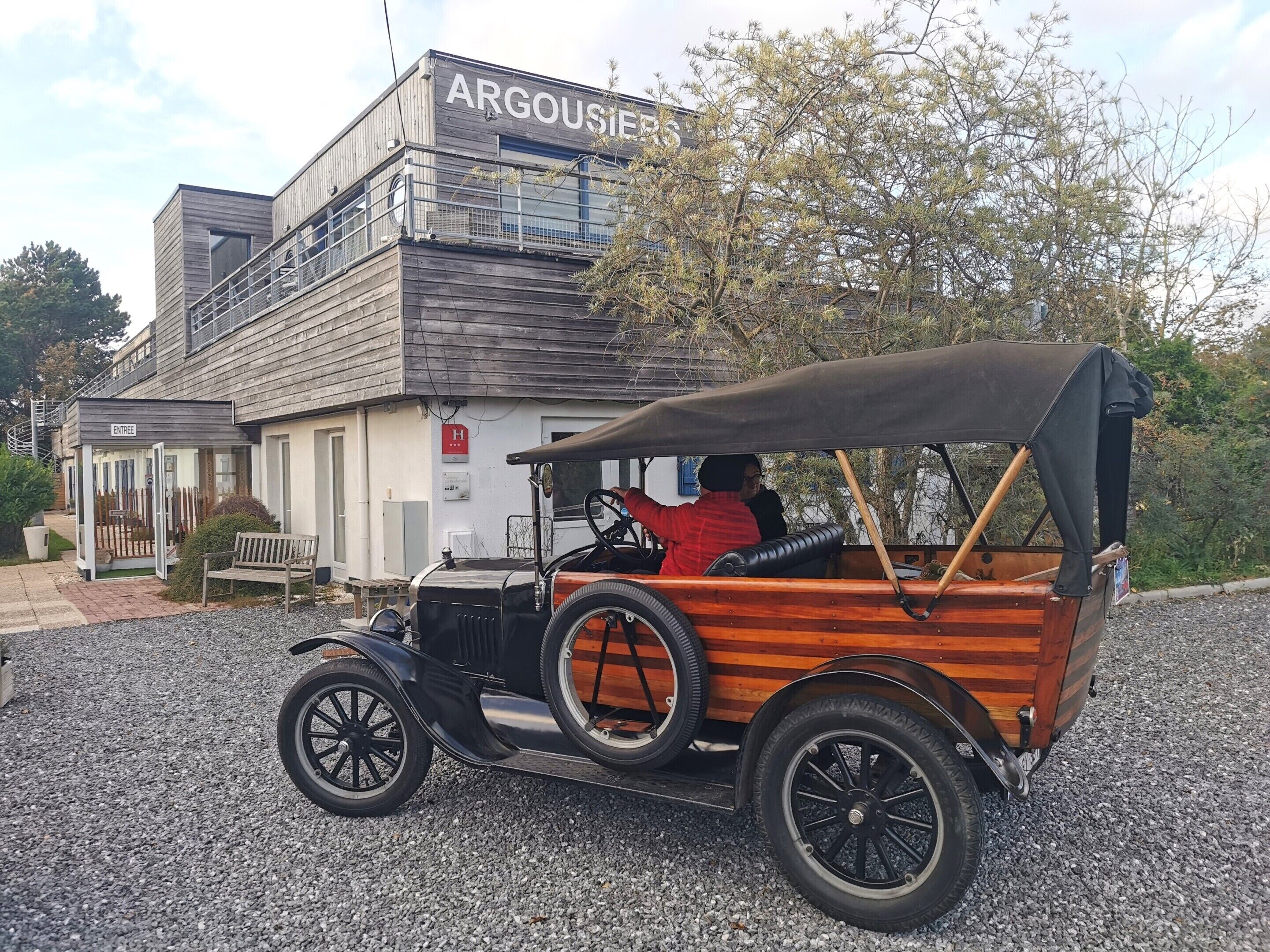 A vintage car parked in front of a building with a sign that reads "ARGOUSIERS".