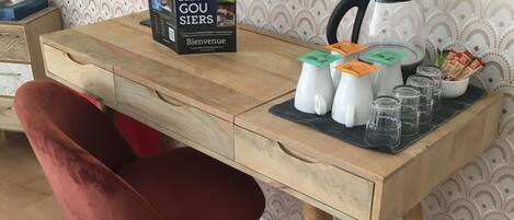 Un pupitre de madera con una silla roja, una cafetera y un folleto de bienvenida.