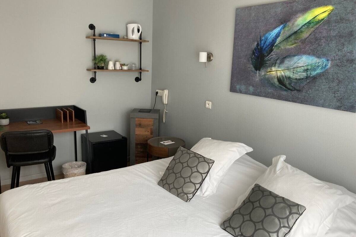 A neatly arranged hotel room with a bed, a desk, a chair, and a small table.