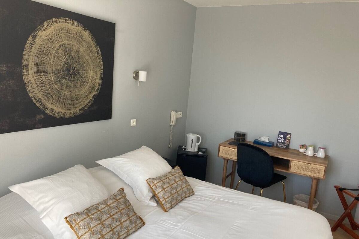 A hotel room with a large bed, a desk, a chair, and a wall-mounted artwork.