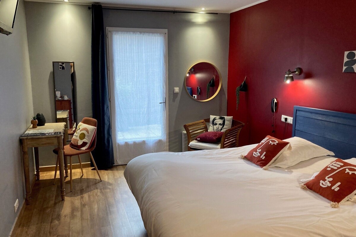 A hotel room with a bed, a desk, a chair, a mirror, and a red wall.