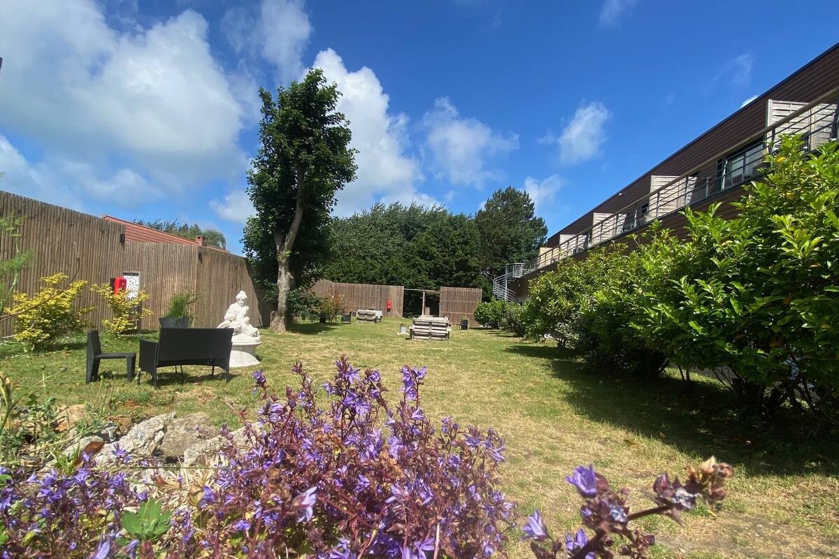 A backyard with a wooden fence, a statue, a bench, and a flower bed.