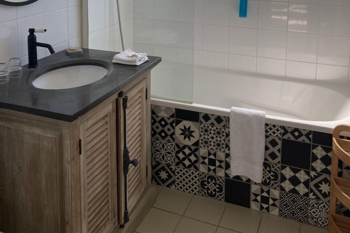 A bathroom with a sink, mirror, shower, and a window.