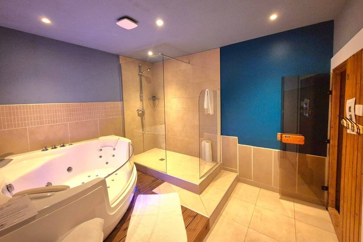 A modern bathroom with a large bathtub, a glass-enclosed shower, and a wooden door.