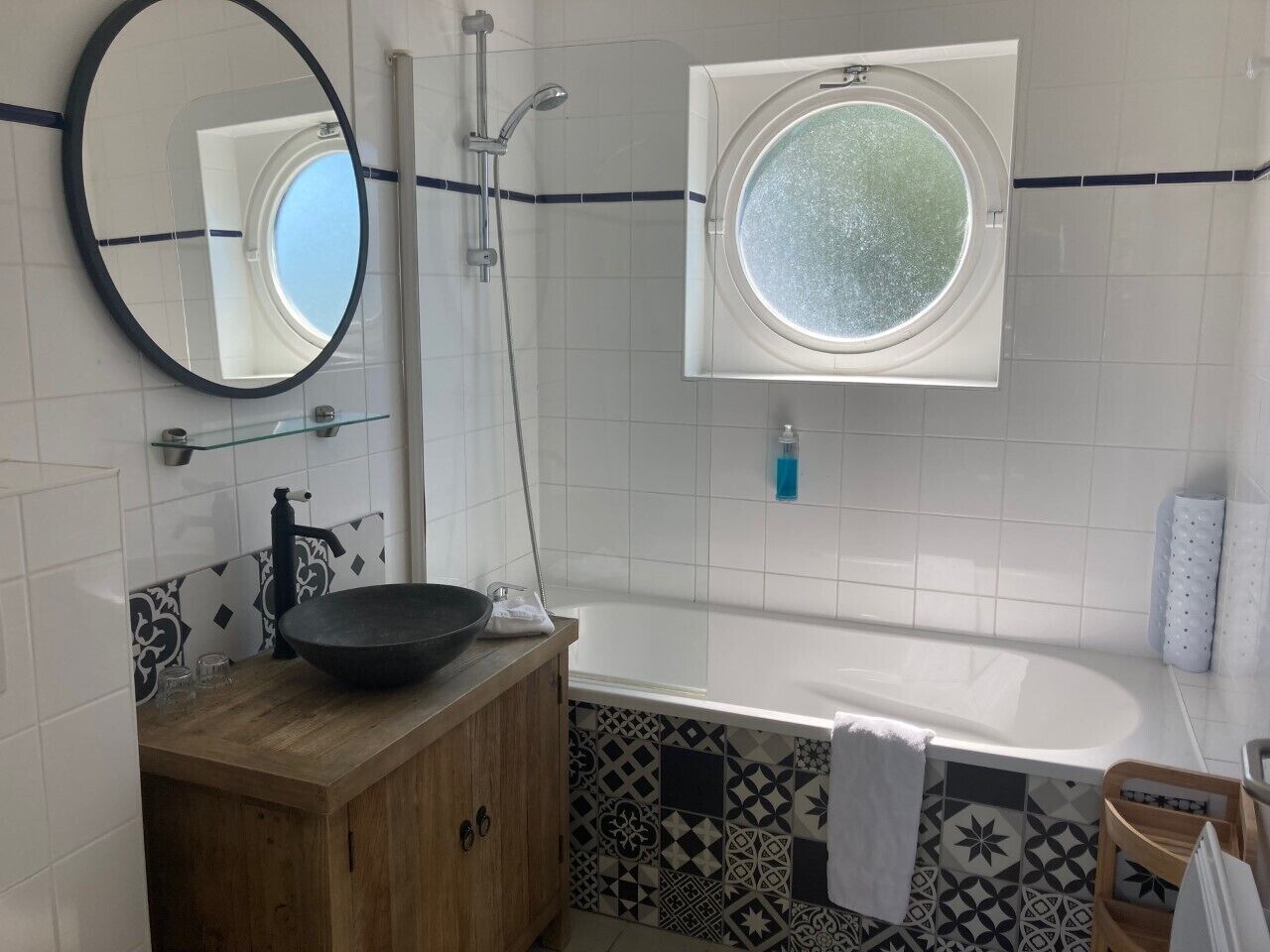 Um banheiro com banheira, espelho redondo, pia com cuba preta e azulejos estampados.