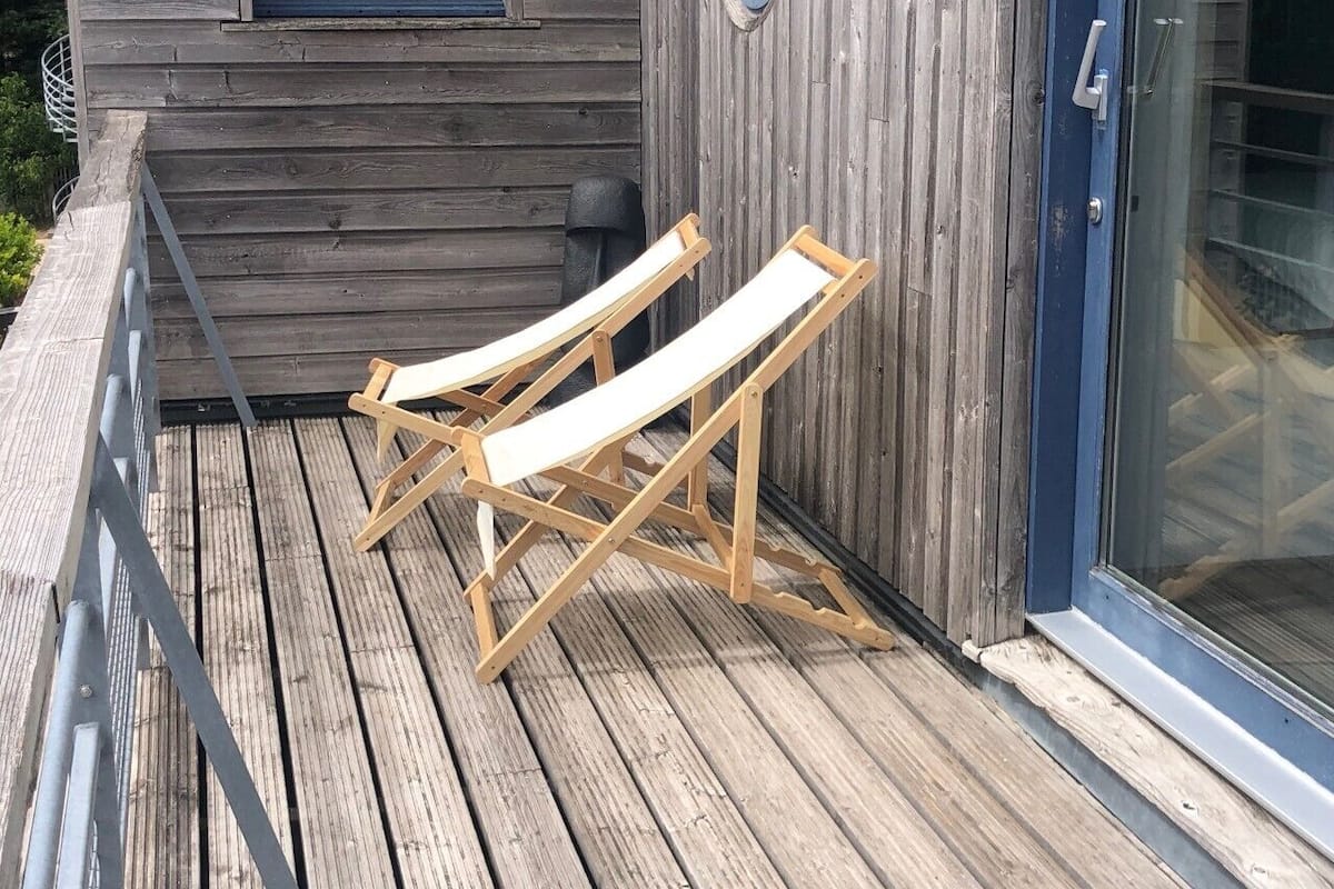 Zwei Holzliegen auf einer Holzterrasse mit Glastür und Fenster.