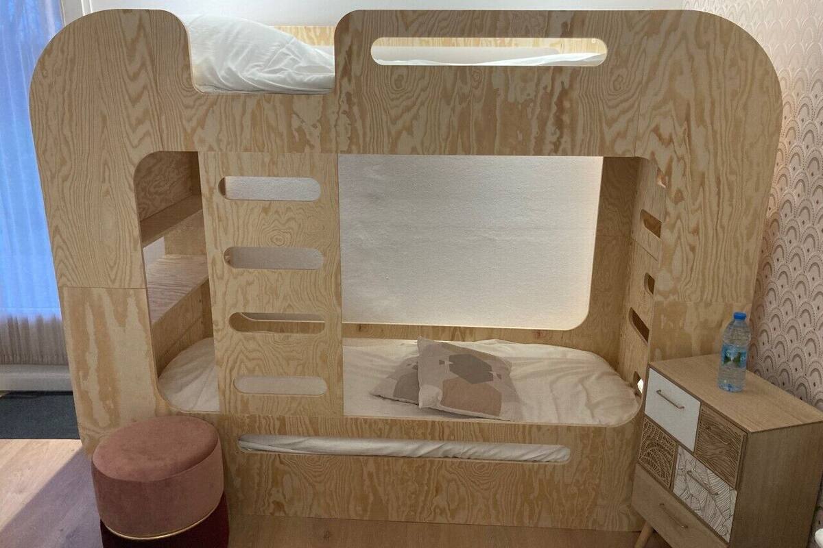 A wooden bunk bed with a storage drawer and a small bedside table.