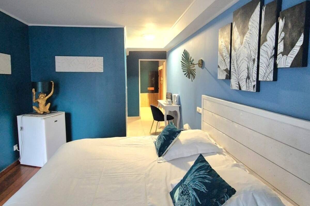 A hotel room with a large bed, a desk, and a chair. There is a small refrigerator and a decorative plant on the desk.