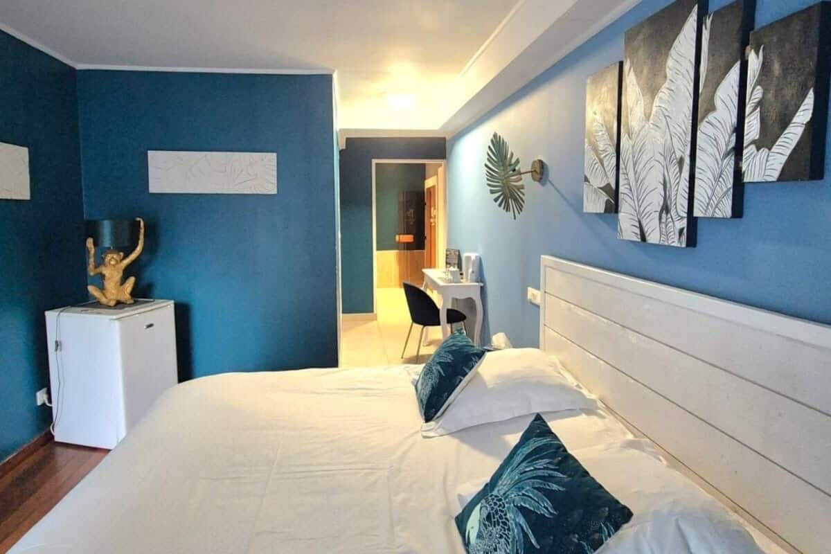 Ein Hotelzimmer mit einem großen Bett, einem Schreibtisch und einem Stuhl. Auf dem Schreibtisch befindet sich ein kleiner Kühlschrank und eine Zierpflanze.