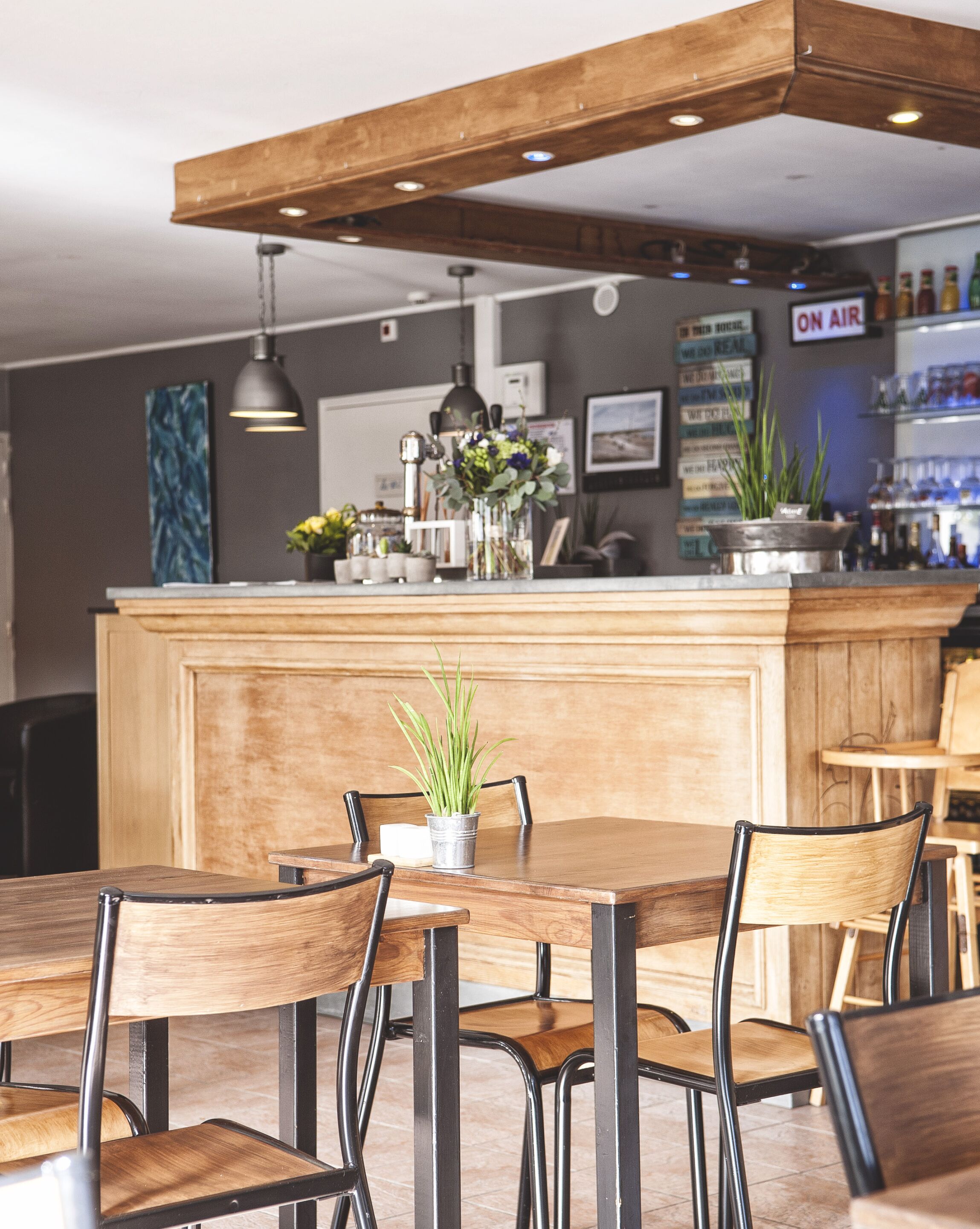 A restaurant interior with wooden tables and chairs, a central counter with a potted plant, and a 'ON AIR' sign.