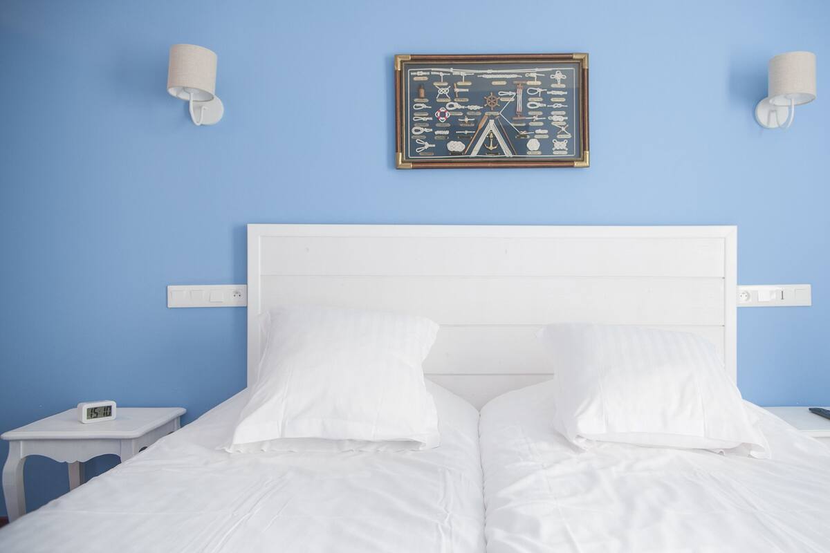 A bed with white bedding, two nightstands with clocks, and a framed nautical chart on the wall.