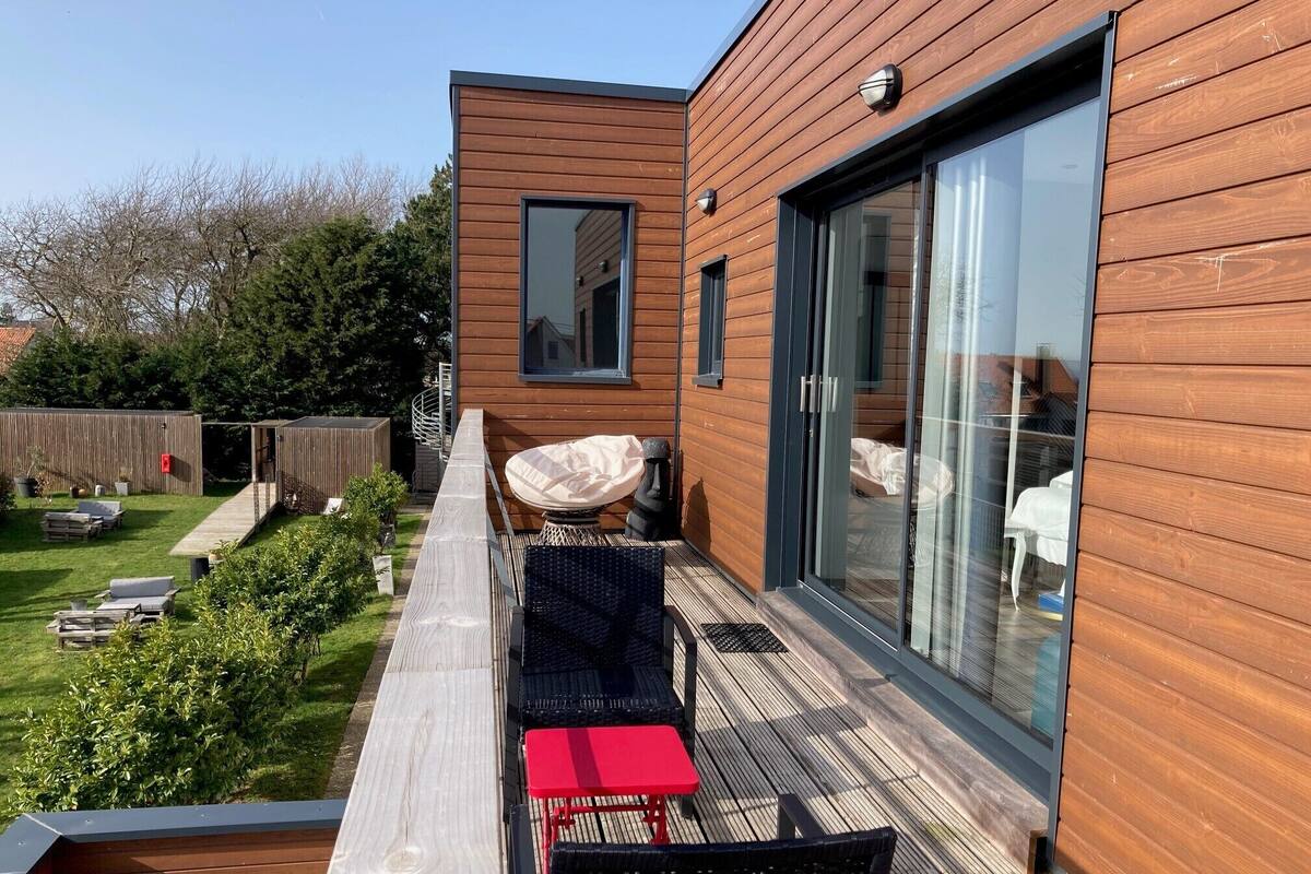 A modern outdoor deck with a wooden deck, a red table, and two black chairs.