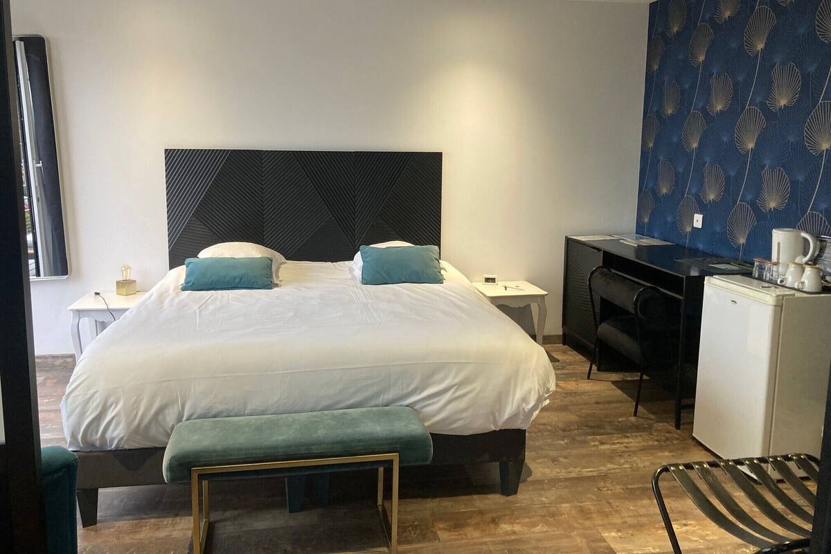 A hotel room with a bed, a desk, a chair, and a small refrigerator.