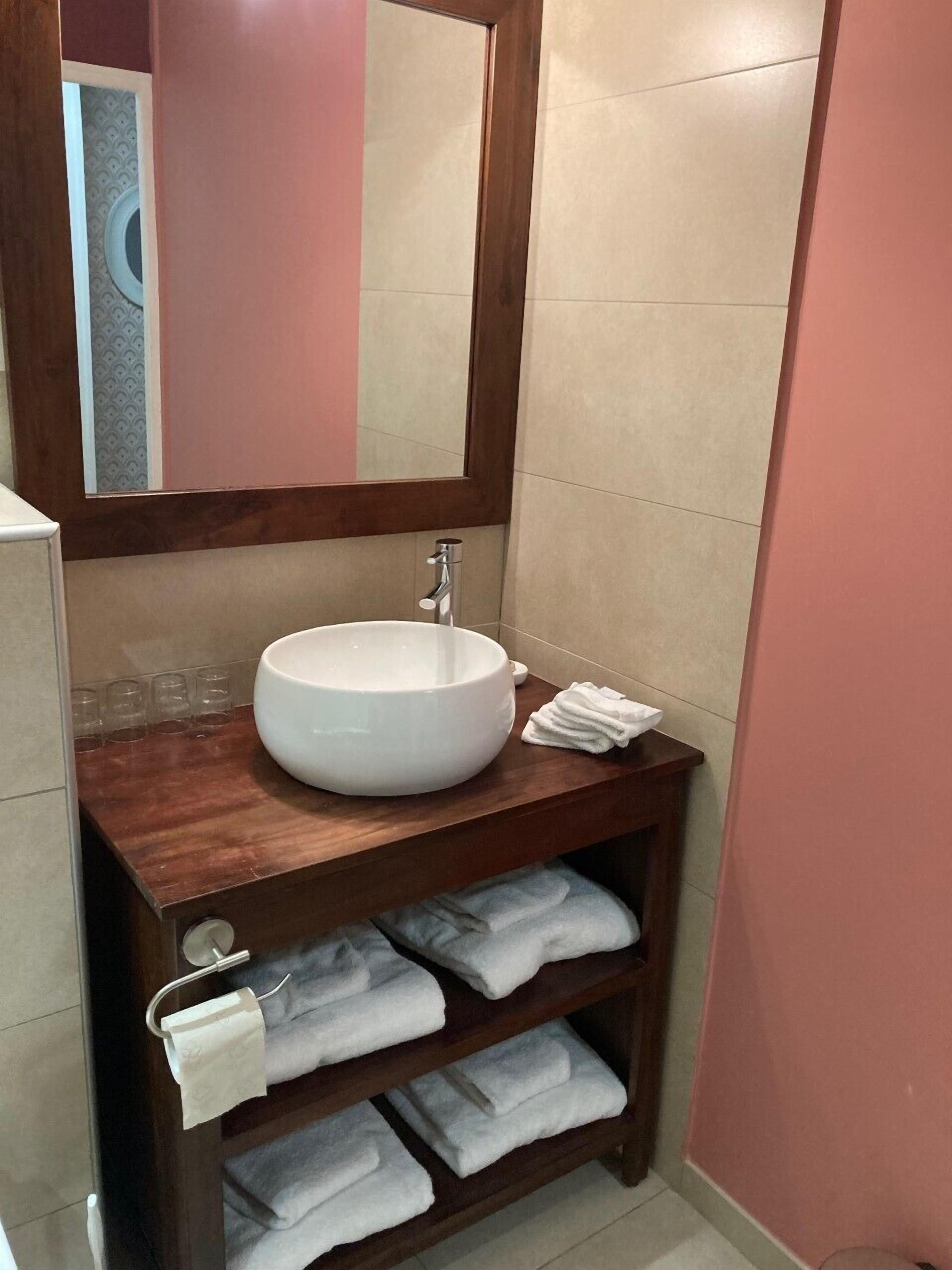 Un bagno con un ampio lavandino bianco, uno specchio sopra e un mobile contenitore in legno con ripiani pieni di asciugamani.