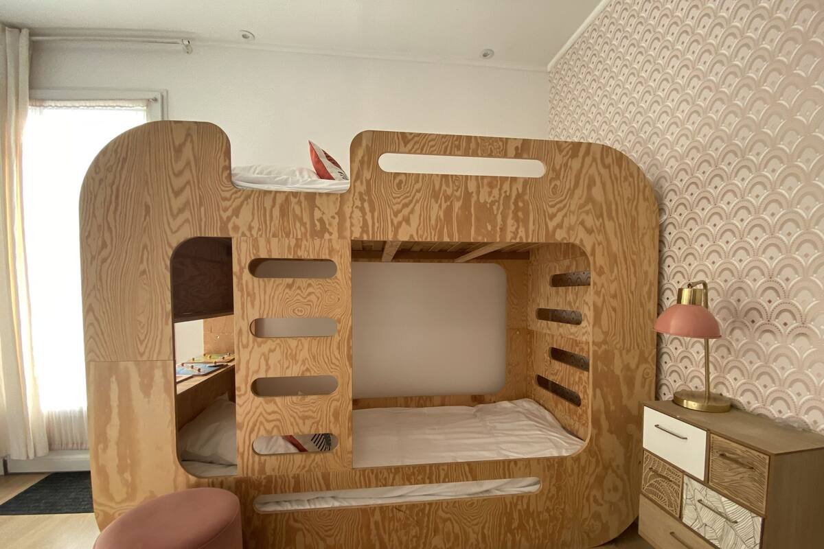 A bunk bed with a desk and drawers, a pink chair, and a lamp on a dresser.