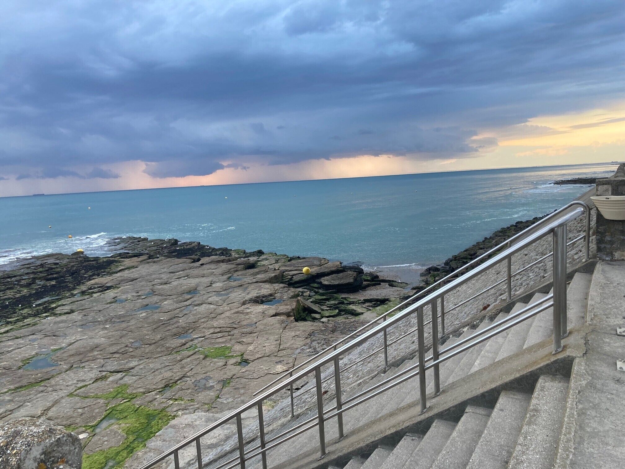 A coastal staircase leading to a rocky shoreline with a view of the sea and stormy sky.