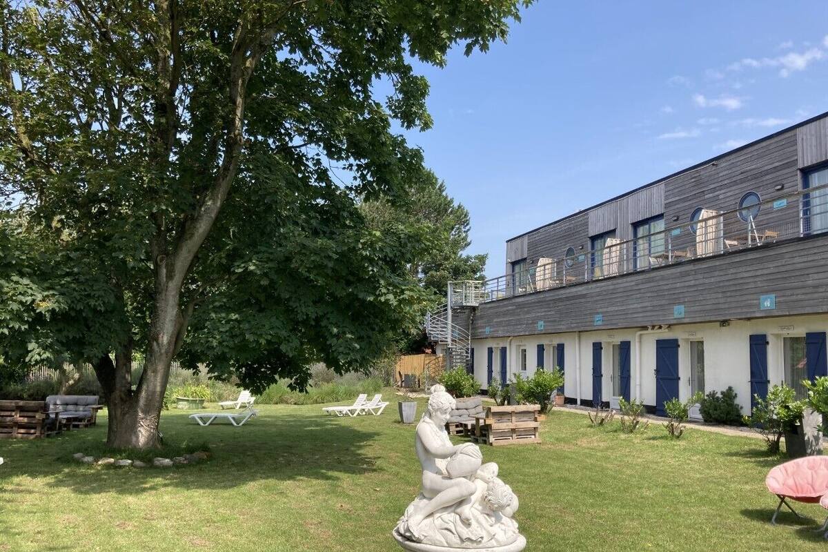 A building with a row of rooms, a lawn with a statue, and a tree.