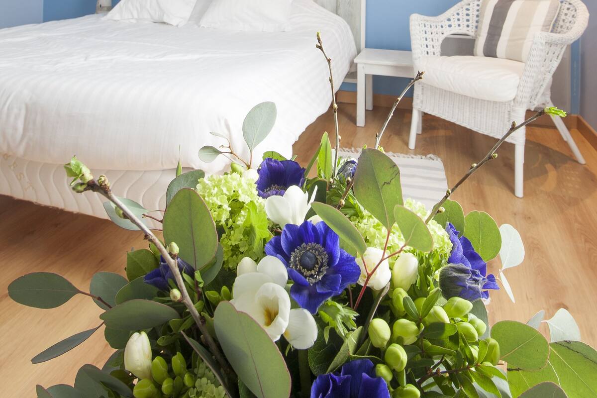 A bedroom with a bed, a chair, a nightstand, a wall-mounted lamp, and a painting.