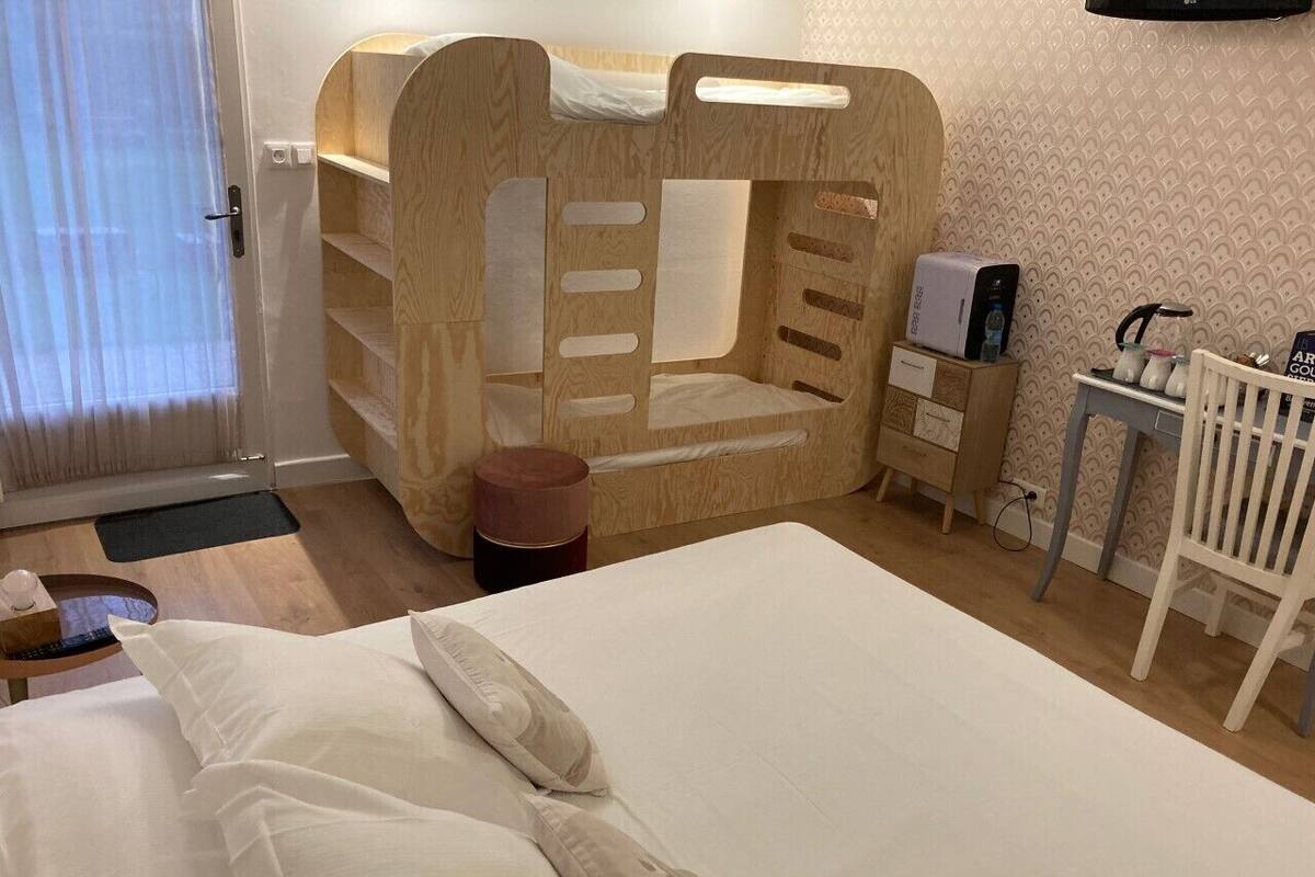 A hotel room with a large bed, a wooden bunk bed, a small table with a kettle, and a chair.