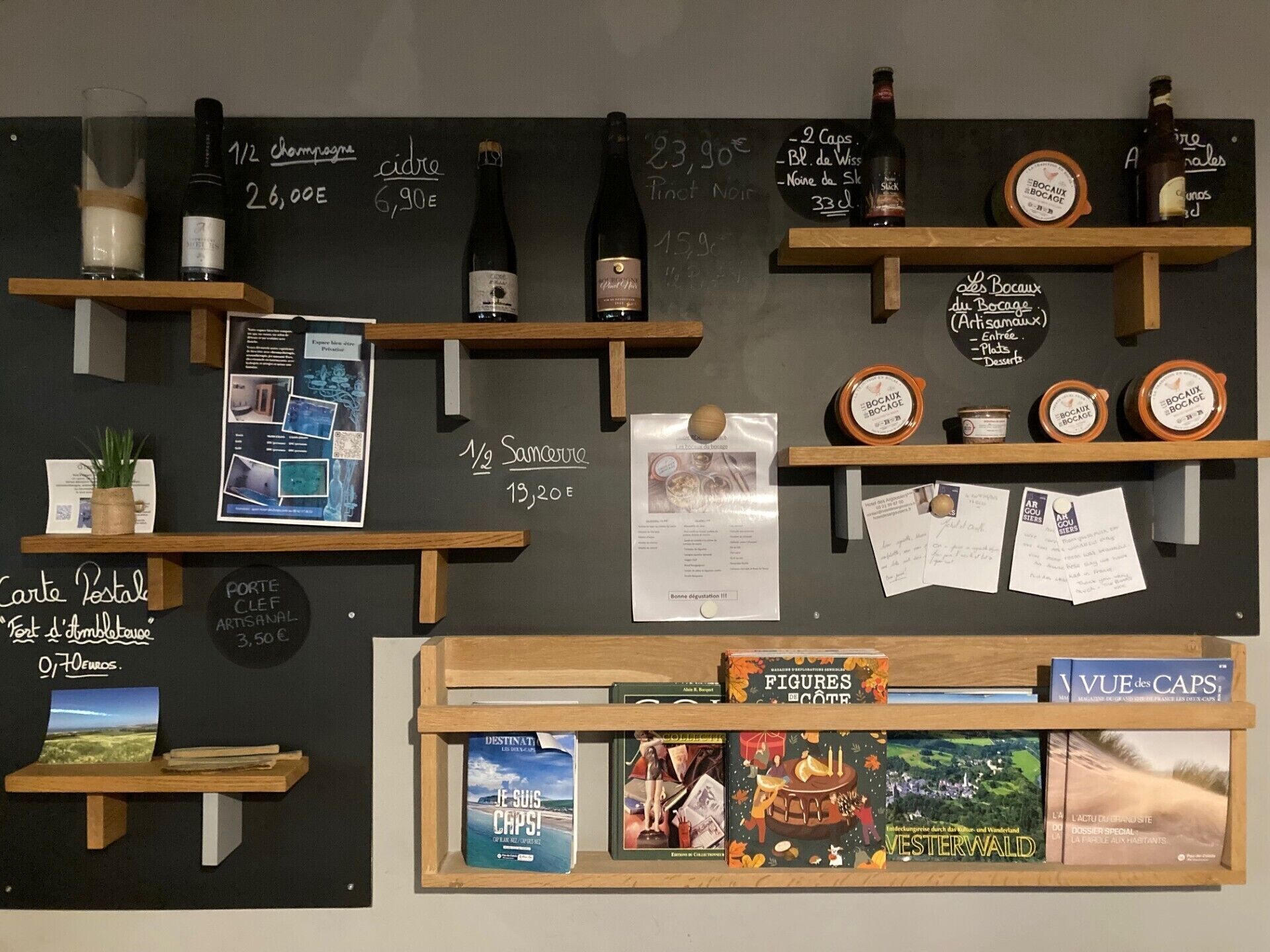 A wall with various items displayed, including bottles, books, and a chalkboard with prices and descriptions.