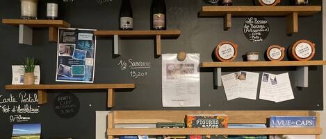 A wall with various items displayed, including bottles, books, and a chalkboard with prices and descriptions.