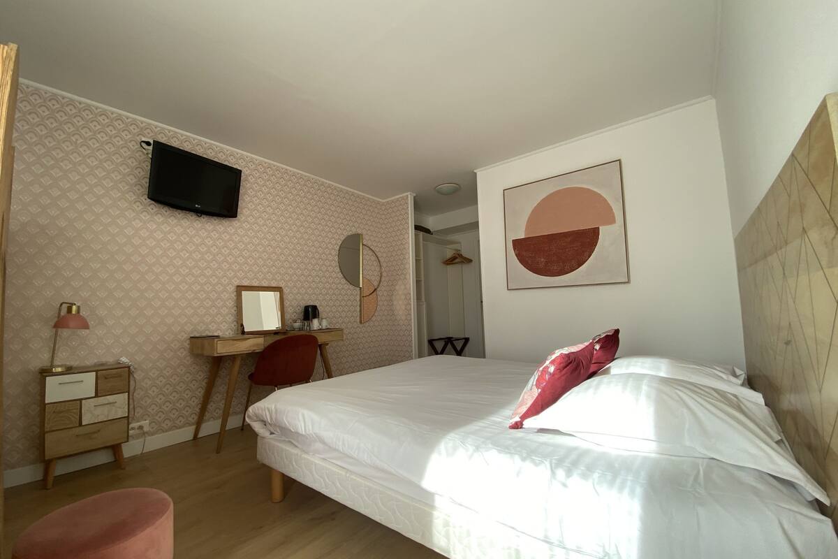 A bedroom with a bed, a desk, a chair, a TV, and a wall with a geometric design.